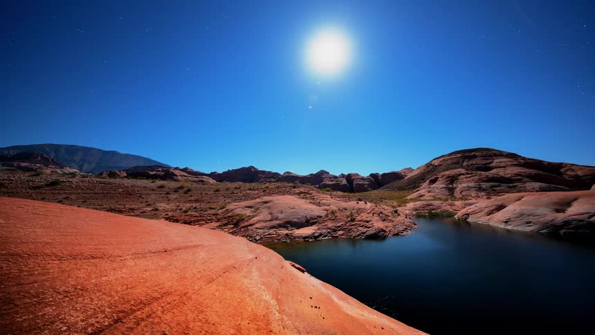The sun moves across the blue sky over canyon rock and water