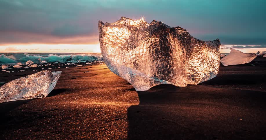 Pieces of ice on the sand glow as they reflect the golden sunlight at sunset