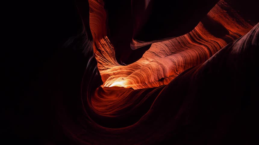 Sunlight can be seen at the end of a rock tunnel that shows several layers of sediment