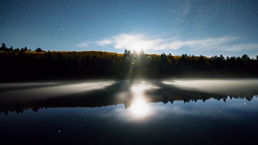 The smooth blue surface of the water reflects the trees and sky from day to night