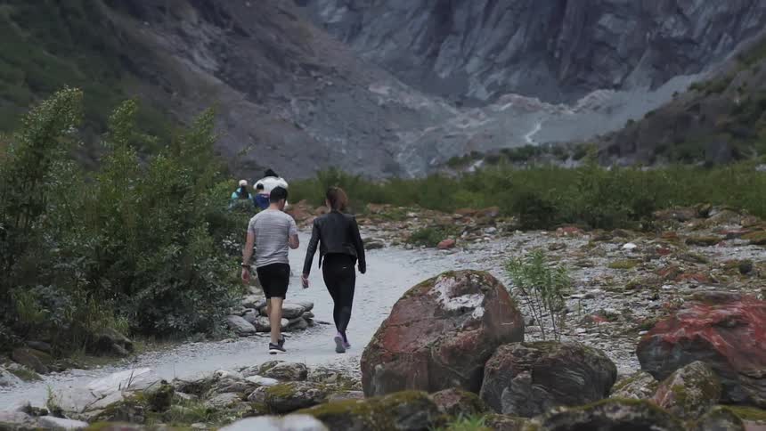 People walk along a sandy path to the rocky hills