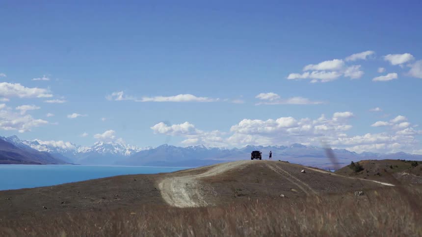 Winding is blowing grass by the coast of a large lake with mountains in the distance