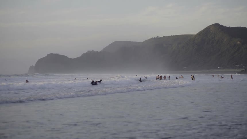 Surfers ride waves near the shoreline on a misty, foggy day at the sea.