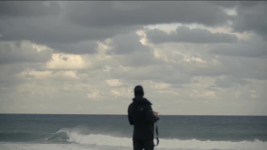 A person standing on a beach as wave rolls in on a cloudy day