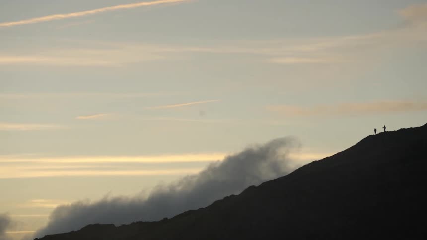 Two people watch the smoke at the top of the mountain