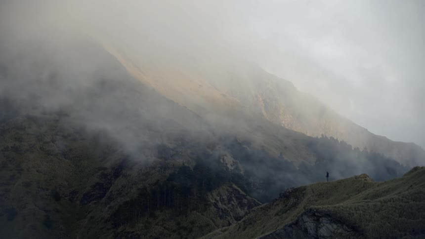 A person standing on a cliff with mountains in the background
