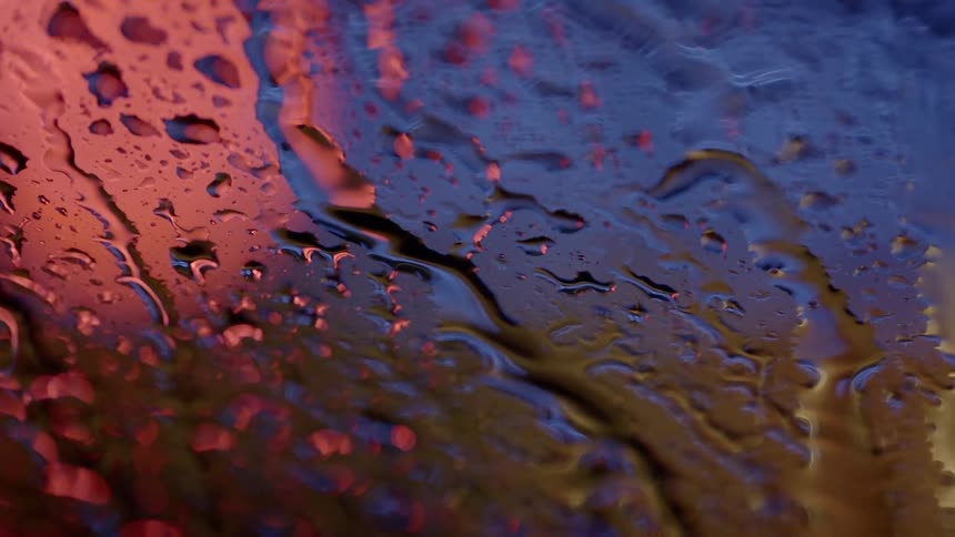Rivulets of rain run a windshield in rush hour traffic
