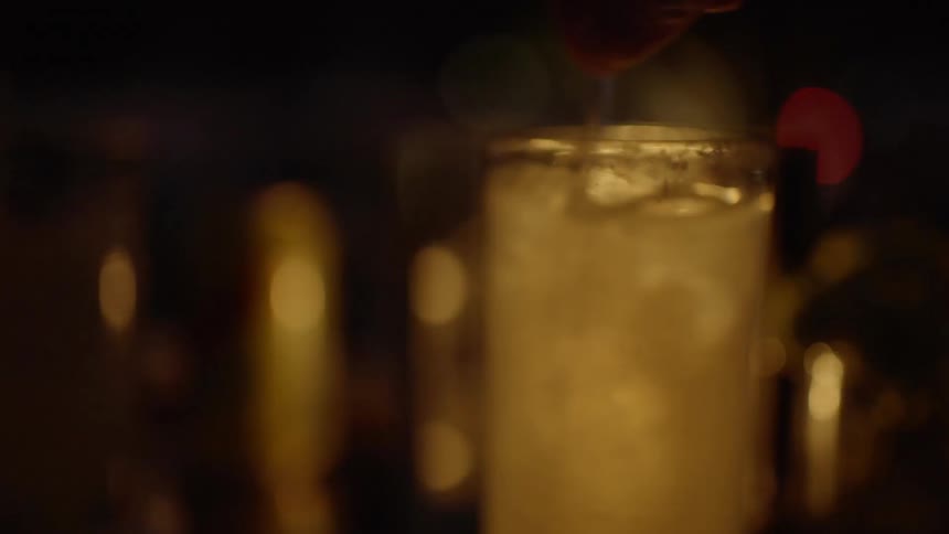 A person stirs a mixed drink with a swizzle stick at night