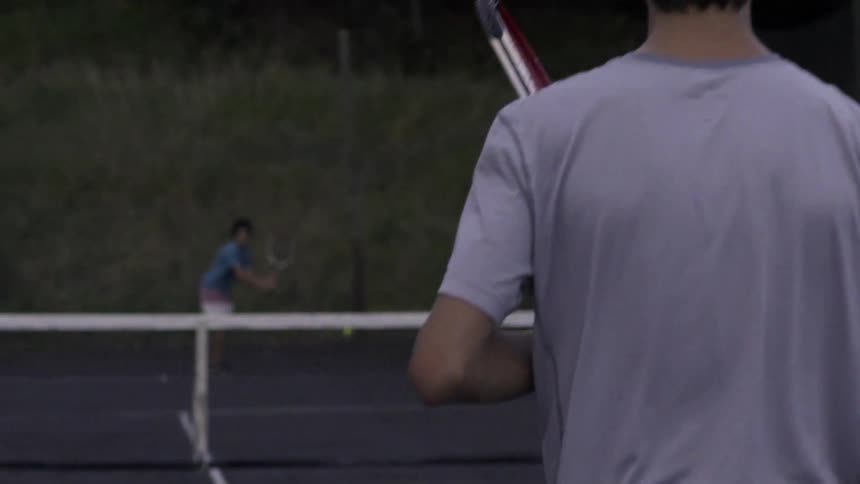 Two people playing tennis on a court at sunset