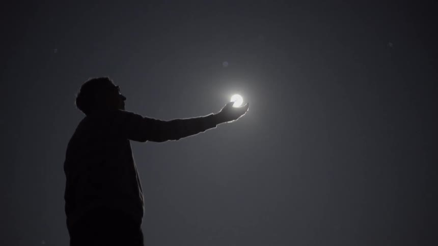 A man holds his hand out as if he is catching the moon with it