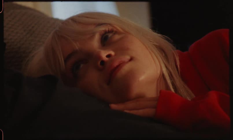 A blonde haired females rests her head on her male companion as they lay down indoors