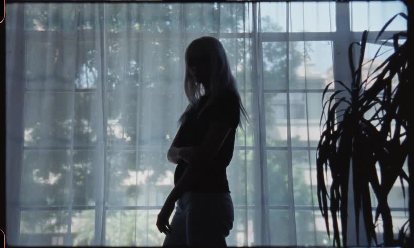 A woman poses in front of a window that has translucent curtains