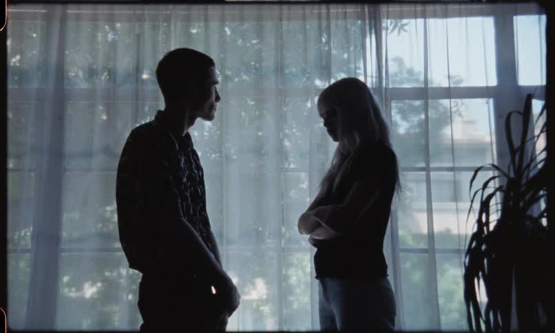 Young couple looking sad while talking in front of a large window