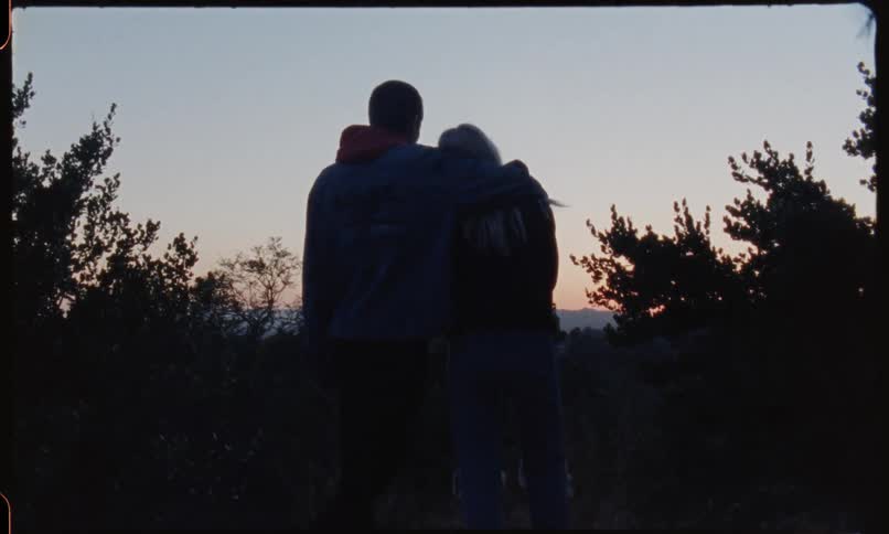 Two people hug at sunset on a hill