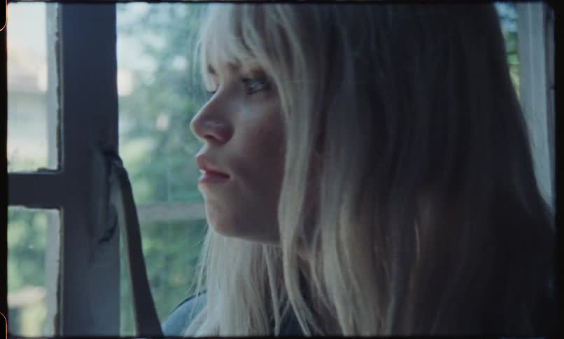 Sad blonde haired girl smoking looking out a window