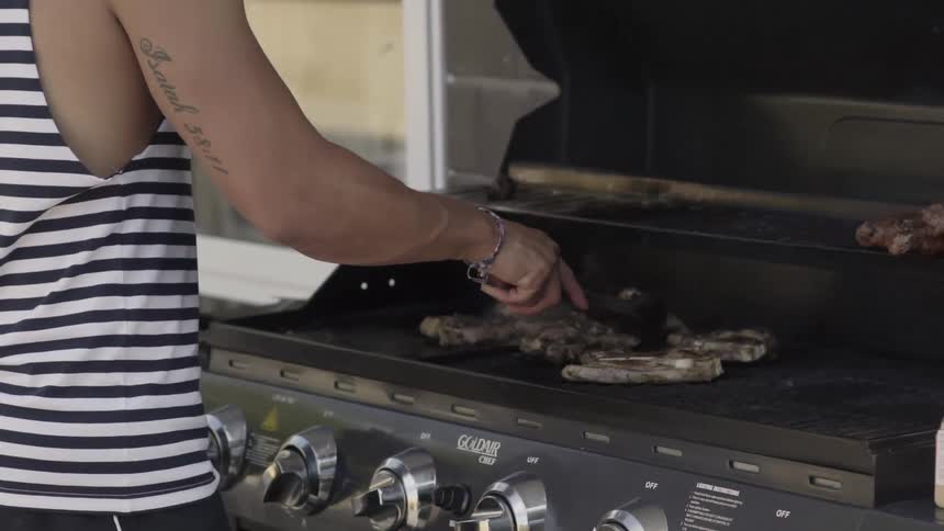 Person Turning Meat on Outdoor Grill While Cooking Food Over Open Flame.