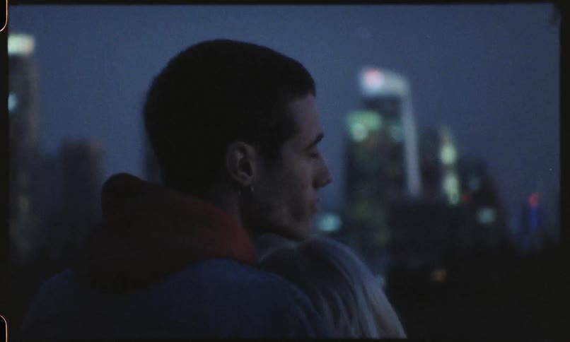 Couple stand hugging in front of night cityscape