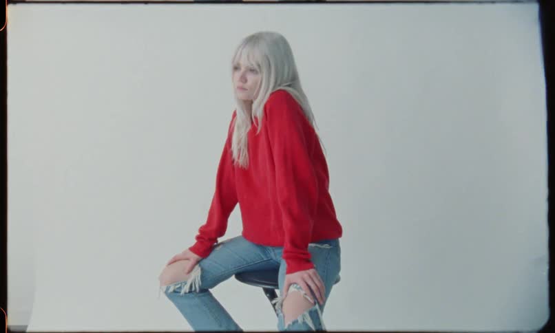 Blonde female wearing red sweatshirt and torn denim jeans at photo shoot