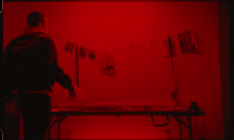 A man rips hanging photos down in a darkroom
