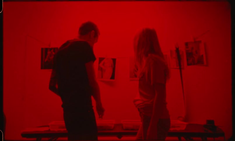 A man and a woman talk while standing a photography darkroom