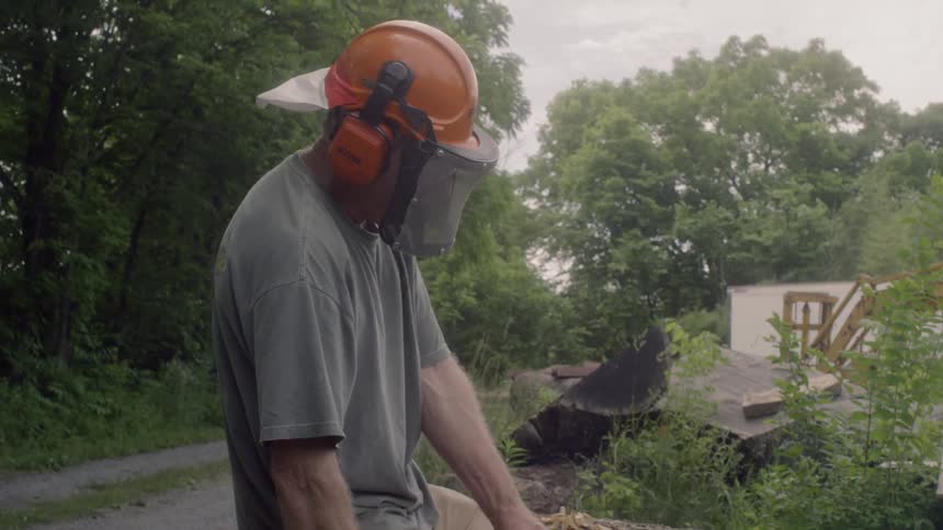 A man in a safety helmet cuts a fallen tree with a chainsaw