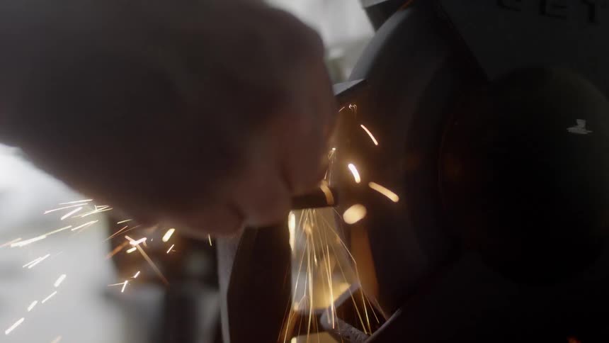A man uses a tool to shave metal which causes sparks to fly