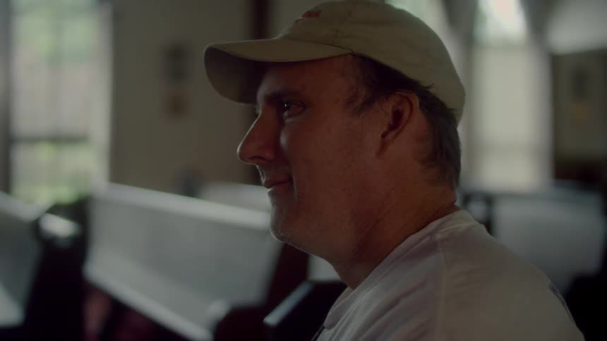 A man sits in a church and stands up from the pew