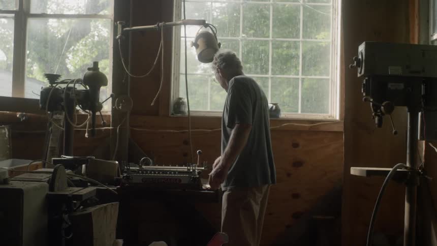 A man walks through his workshop past his drill press to his lathe