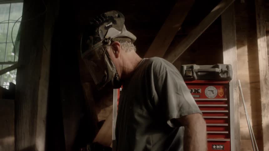 A man with a helmet and mask walking in a workshop with toolboxes in the background
