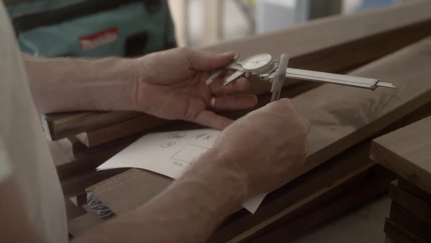 A person writes on a piece of paper and holds a measuring tool in the other hand