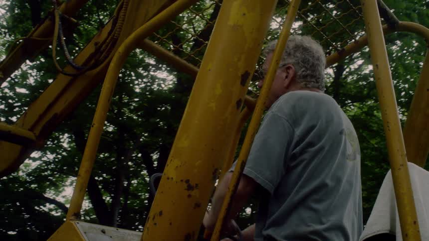 A man driving a crane with trees and the sky in the background