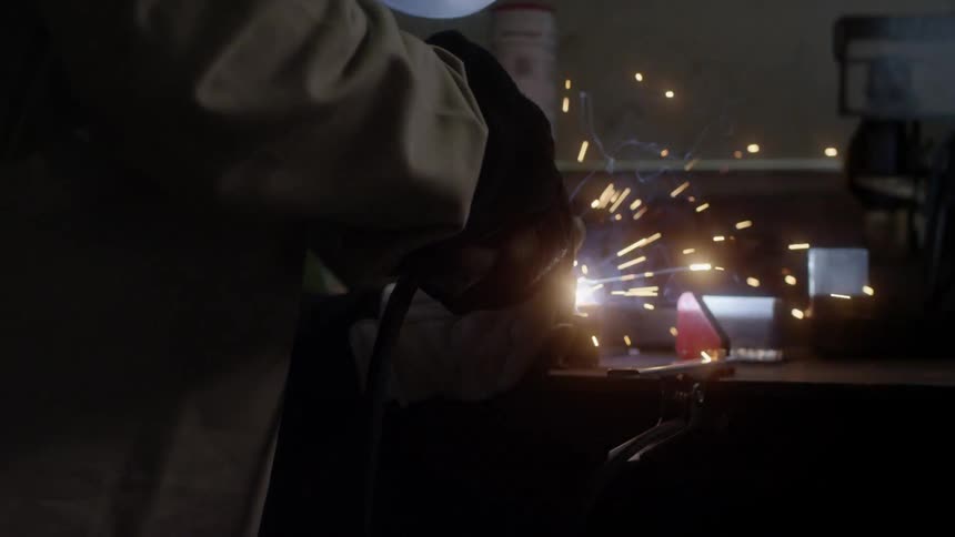 A welder works in a dark shop using a welding machine