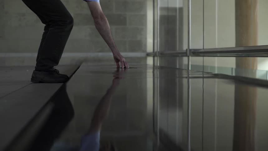 A man runs his fingers through a still pool of water inside a building