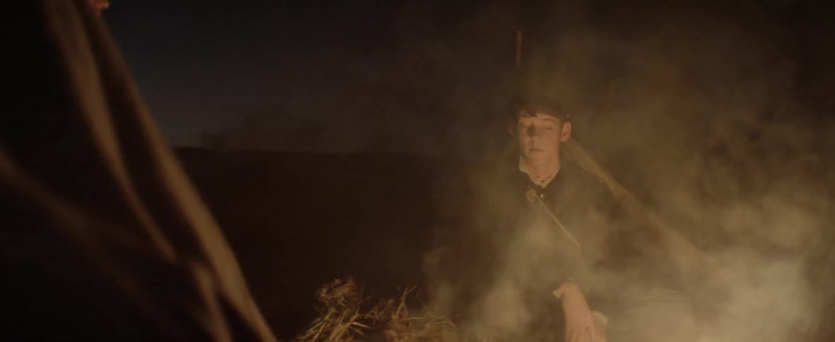 Two people talk to each other in the night while sitting around a bonfire