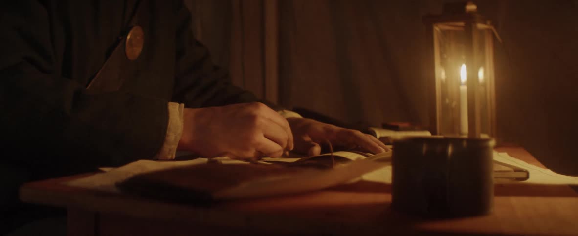 Man writing a letter on a paper under candle light