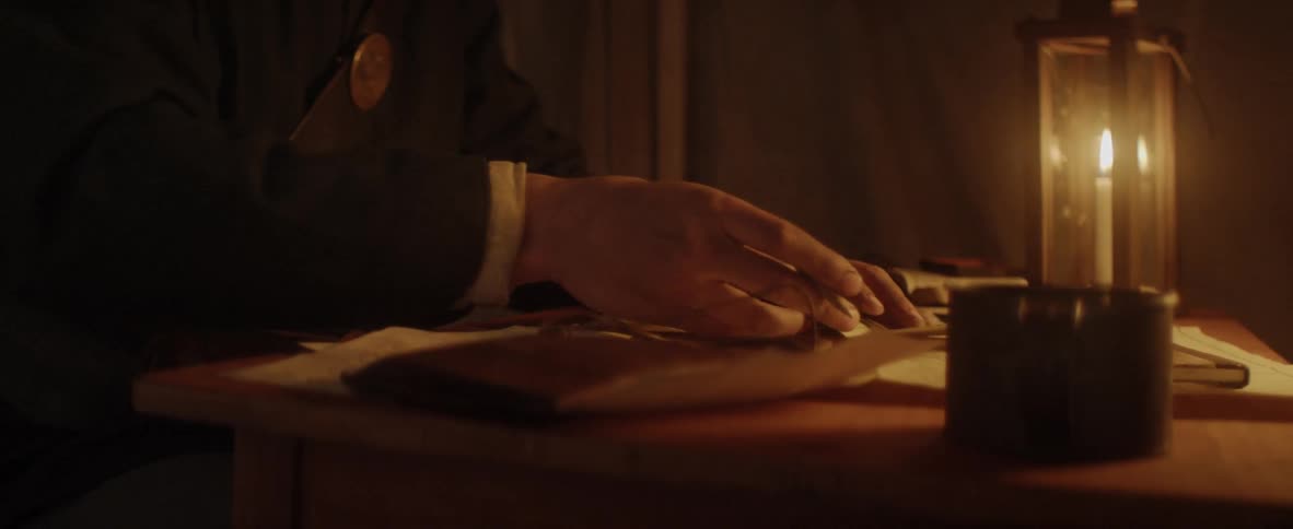 A man sits at a desk and writes by candle light