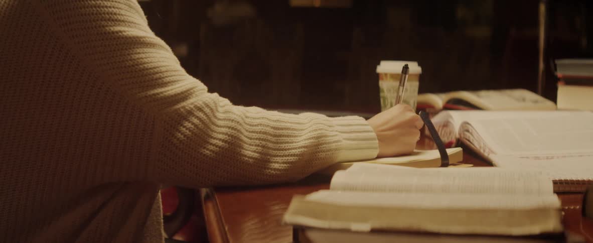 A woman does homework at a desk covered with open books