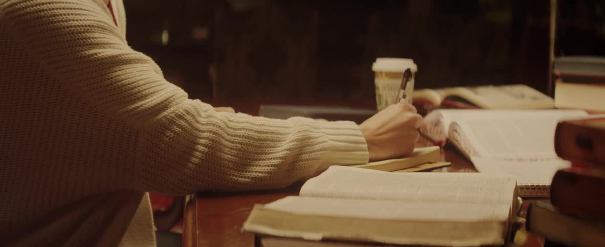 Woman sitting on desk reads book and takes notes