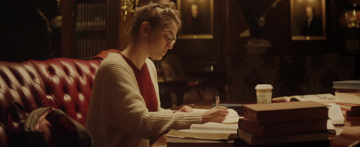 A woman studies and writes at a table cluttered with books