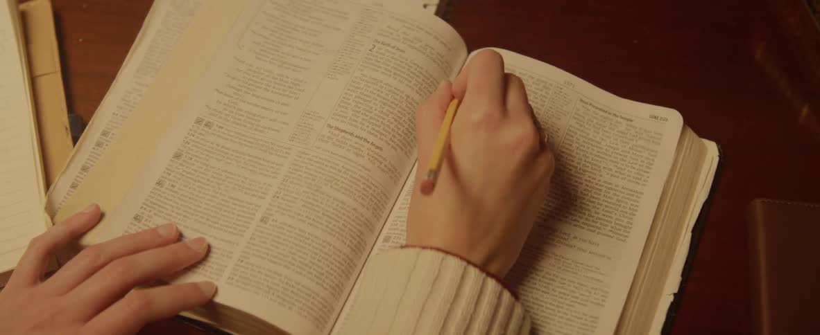 A student underlines a passage in a book using a pencil