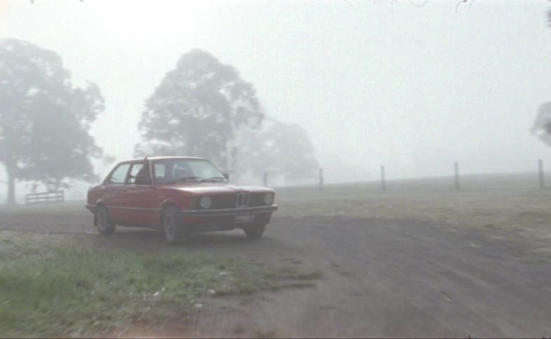 A classic bmw three series is driven on a dirt road on a foggy day