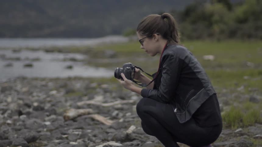 A woman crouches to take a photograph in the wilderness