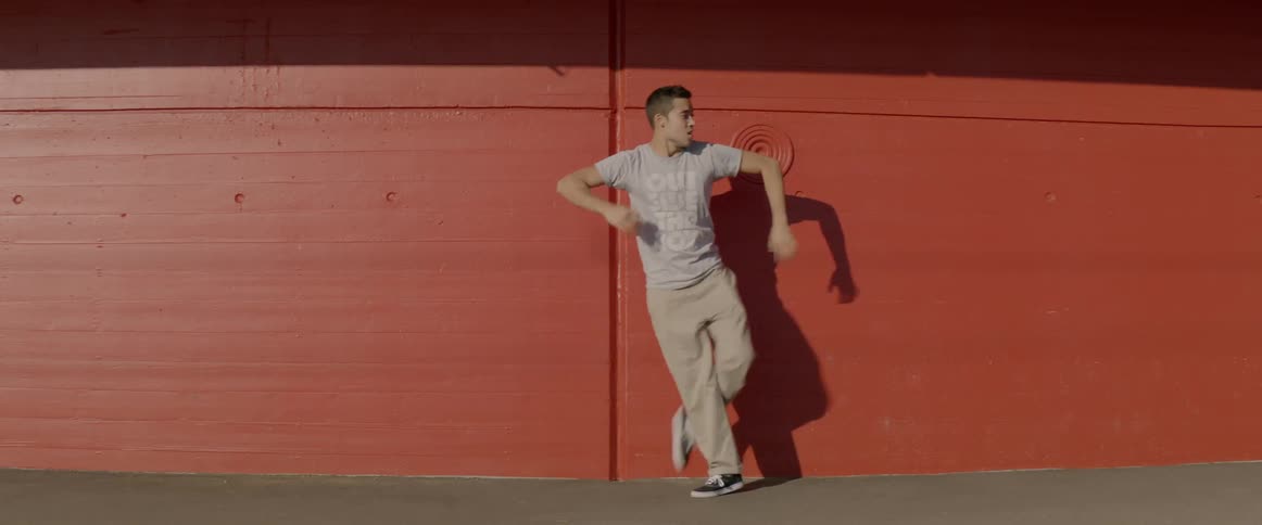 Young man dancing against a red wall outdoors