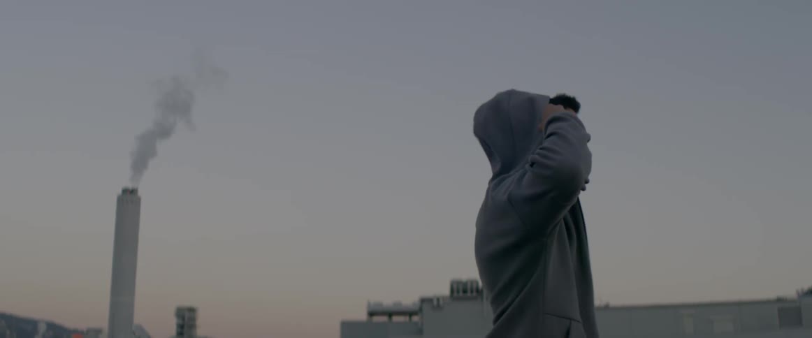 A man standing in an industrial area puts his hood on his head
