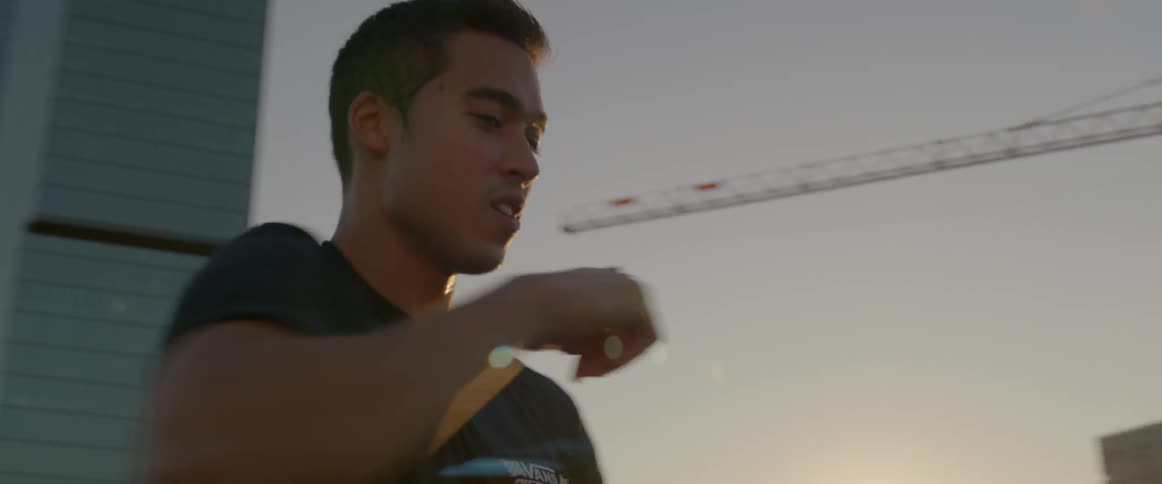 A man dances on a rooftop near cranes
