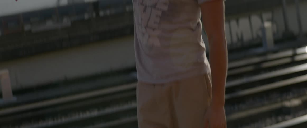 A man dancing outside with train tracks and buildings in the background
