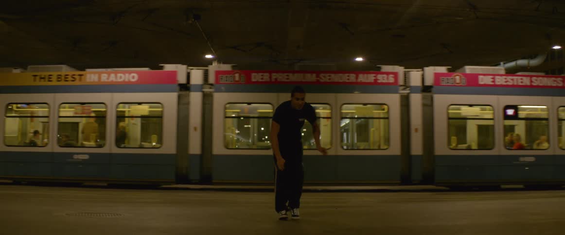 A young man dances in front of an urban train