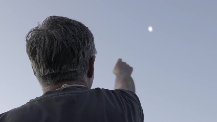 Man Looking and Pointing at Moon in Night Sky With Quiet Outdoor Setting.