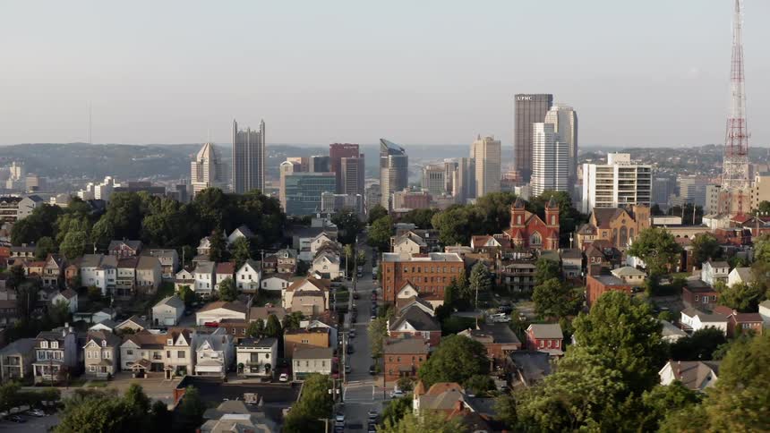 Passing over neighborhood homes buildings and streets with a city skyline behind