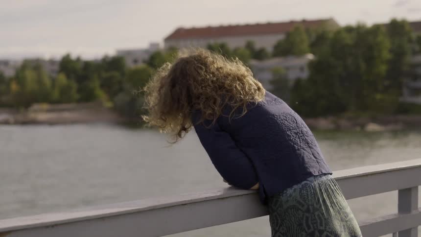 A woman in a blue sweater looks over the side of a bridge